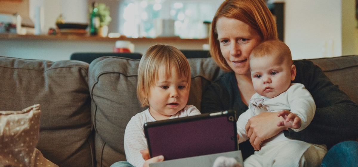 Uma mãe com seus dois filhos segurando um tablet, passando a ideia de que estão verificando a rotina das crianças no Aplicativo Agenda Digital Sloop.